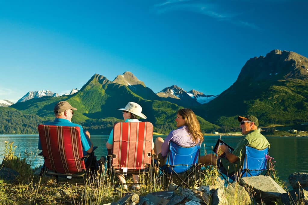 Group of 4 sitting on camp chairs near a lake